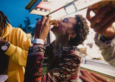 Eine junge Frau, die mit Freunden auf einem Musikfestival Pizza geniesst. | © Gettyimages.com/solstock