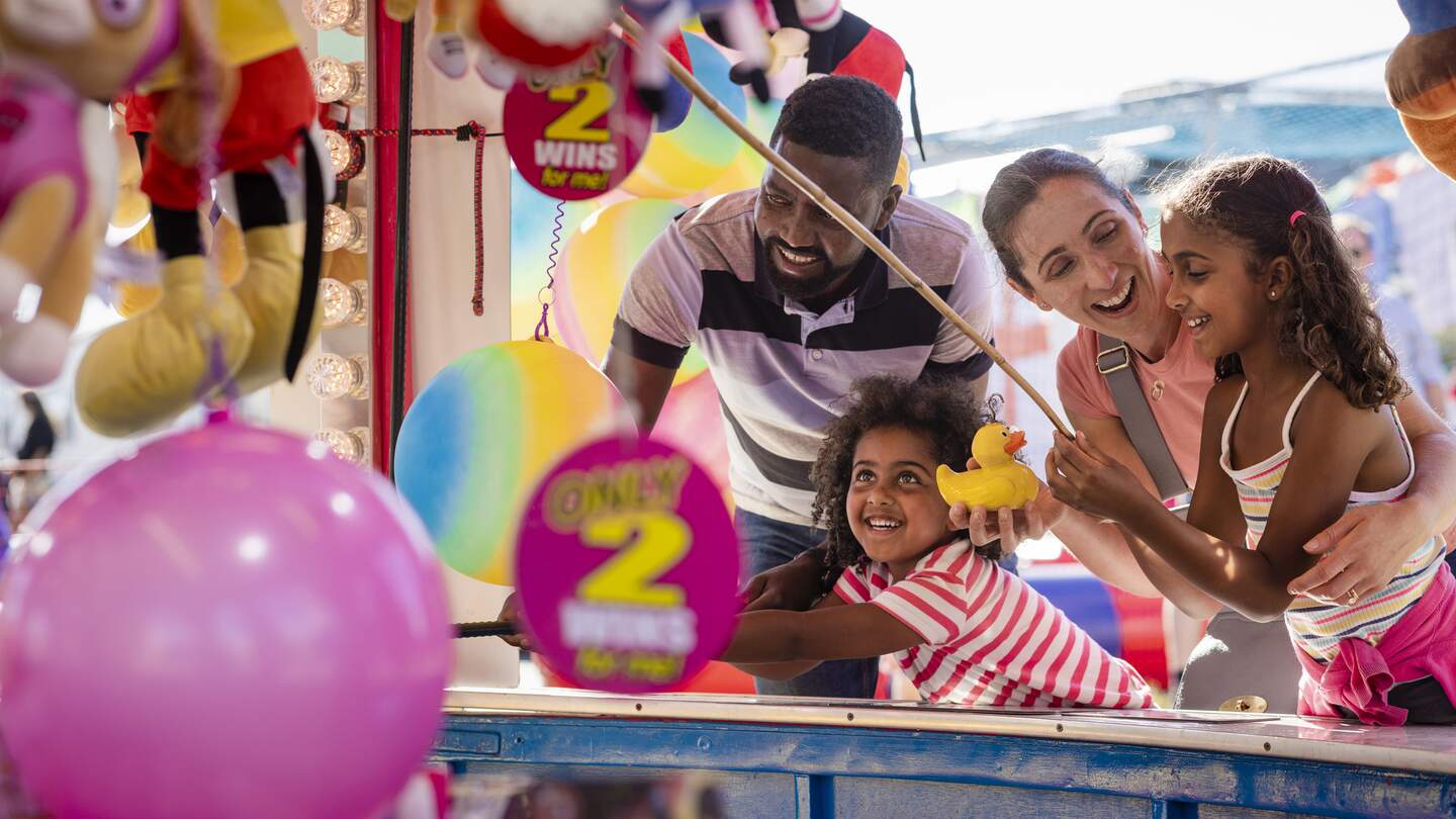 Sie spielen zusammen Entenfang und die Mutter gratuliert ihrer Tochter, nachdem sie erfolgreich eine Ente gefangen hat, um einen Preis zu gewinnen. | © Gettyimages.com/solstock