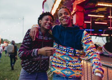 Ein junges Paar laeuft lachend ueber eine Kirmes | © Gettyimages.com/solstock