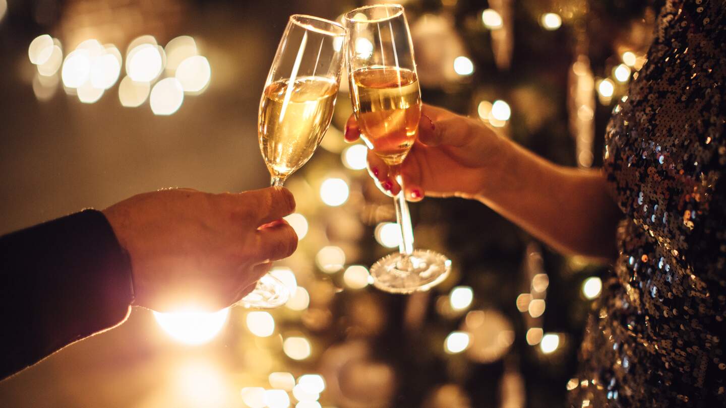 Paar haelt Glaeser Champagner vor dem Weihnachtsbaum | © Gettyimages.com/svetikd