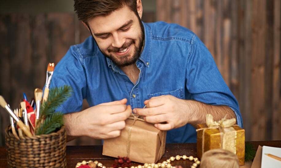 Froehlicher Mann bindet Schnur auf Weihnachtsgeschenk | © gettyimages.com/mediaphotos