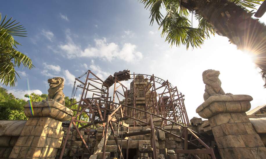 Die Attraktion Indiana Jones (TM) and the temple of peril bei Tag mit Sonne und Palmen | ©  Disney © & TM 2024 Lucasfilm Ltd.