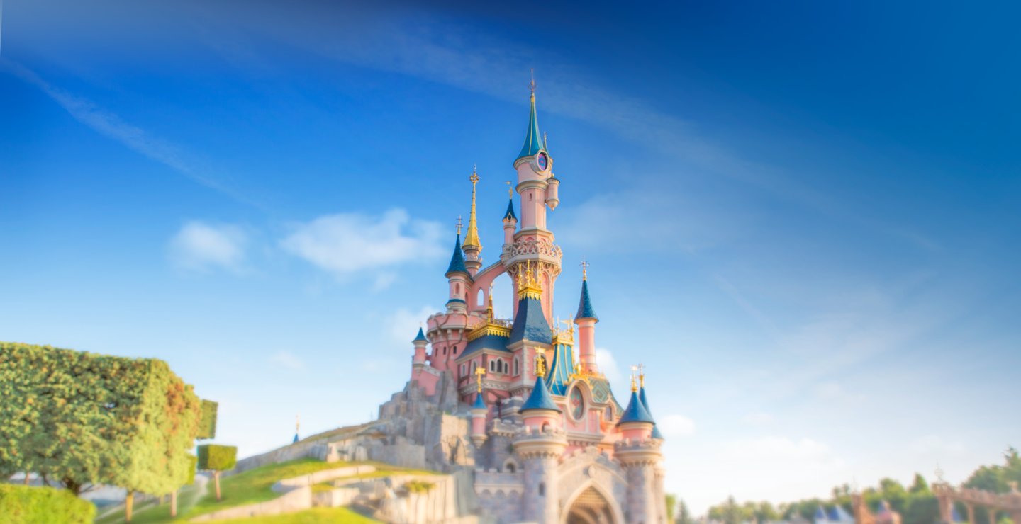 Das rosane Sleeping Beauty Castle mit blauen Tuermen, Fotografiert vom Central Plaza, umgeben von bunten Blumen. | © Disney