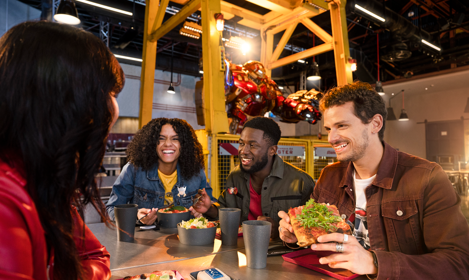 Walt Disney Studios Park Schnellrestaurant Stark Factory Freunde essen Pizza und Pasta. Im Hintergrund ist Hulkbuster. | © 2024 MARVEL.