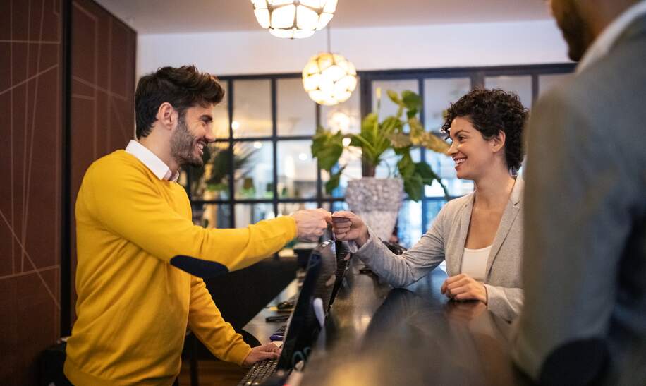  Geschäftsfrau, die im Hotel eincheckt und von einer männlichen Rezeptionistin unterstützt wird. | © Gettyimages.com/alvarez