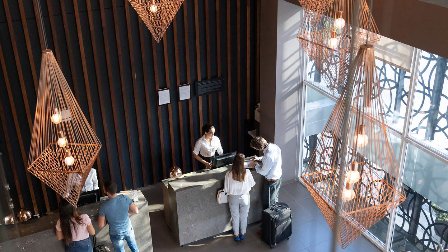 Gruppe von Reisenden checken an der Rezeption eines Luxushotels ein | © Gettyimages.com/Hispanolistic