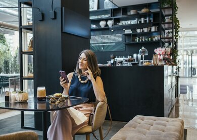 Frau an einem Tisch in der Lobby eines Hotels vor einer Bar | © gettyimages.com/RenataAngerami
