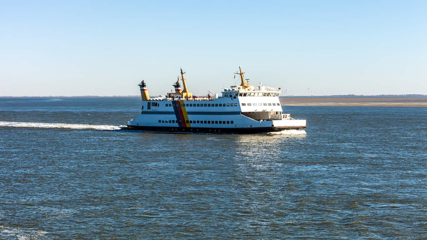Das ganze Bild wird eingenommen von dem Meer. Nur im Hintergrund sieht man einige Windraeder. Im Mittelpunkt steht die Fähre im Zentrum der Aufnahme | © Gettyimages.com/querbeet