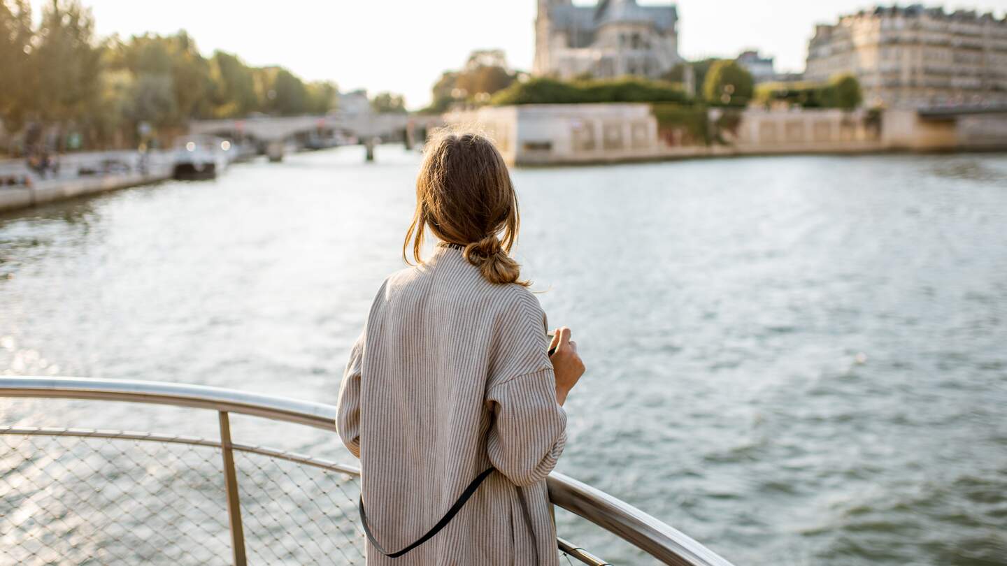 Frau geniesst den Landschaftsblick auf die Stadt Paris vom Boot aus | © Gettyimages.com/RossHelen