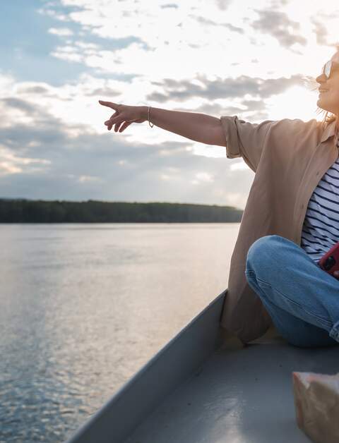 Eine Frau zeigt von einem Boot in die Breitengrade | © Gettyimages.com/Olezzo