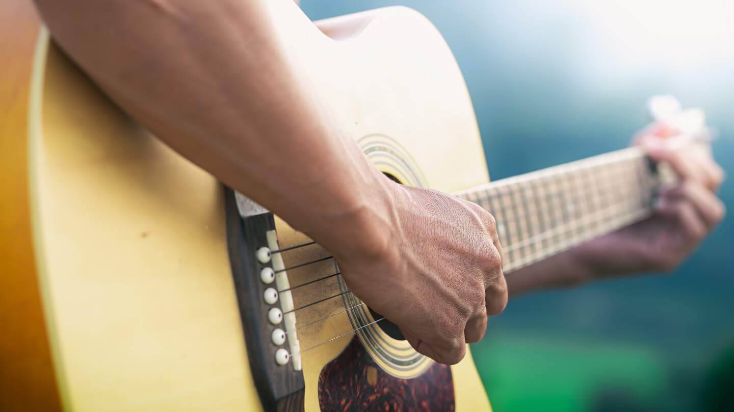 Nahaufnahme eines Gitarrenspielers mit Fokus auf die Gitarre | © Gettyimages.com/ChatkarenStudio