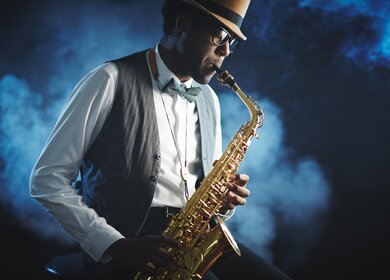Mann spielt mit geschlossenen Augen Saxophon mit blauem nebligem Hintergrund | © Gettyimages.com/shironosov