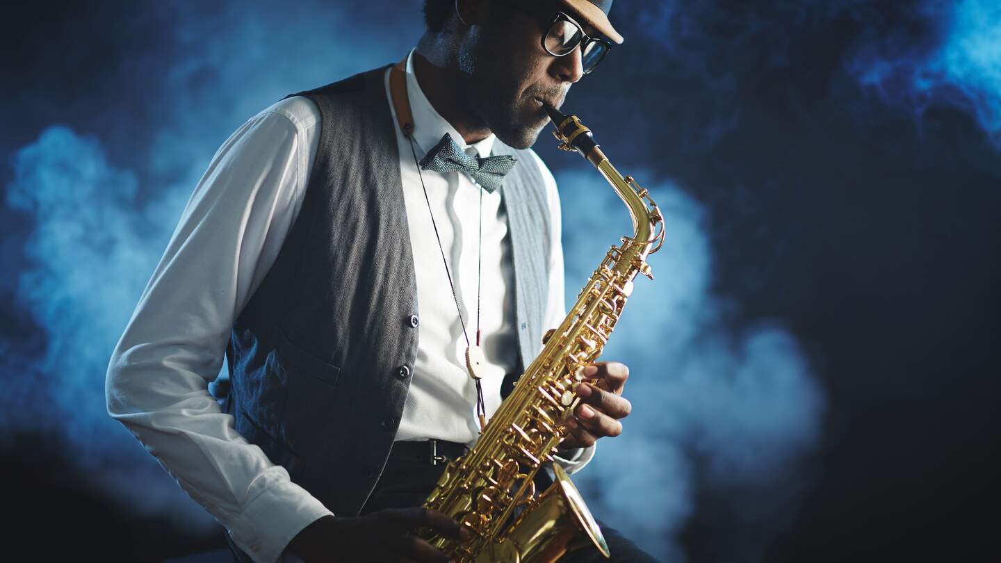 Mann spielt mit geschlossenen Augen Saxophon mit blauem nebligem Hintergrund | © Gettyimages.com/shironosov