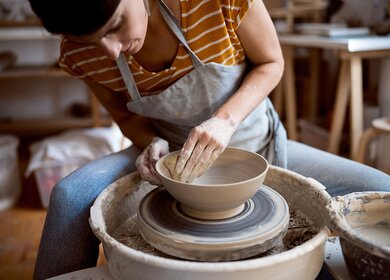 Kaukasische Toepferin, die an der Töpferscheibe in ihrer modernen Werkstatt arbeitet  | © Gettyimages.com/SrdjanPav