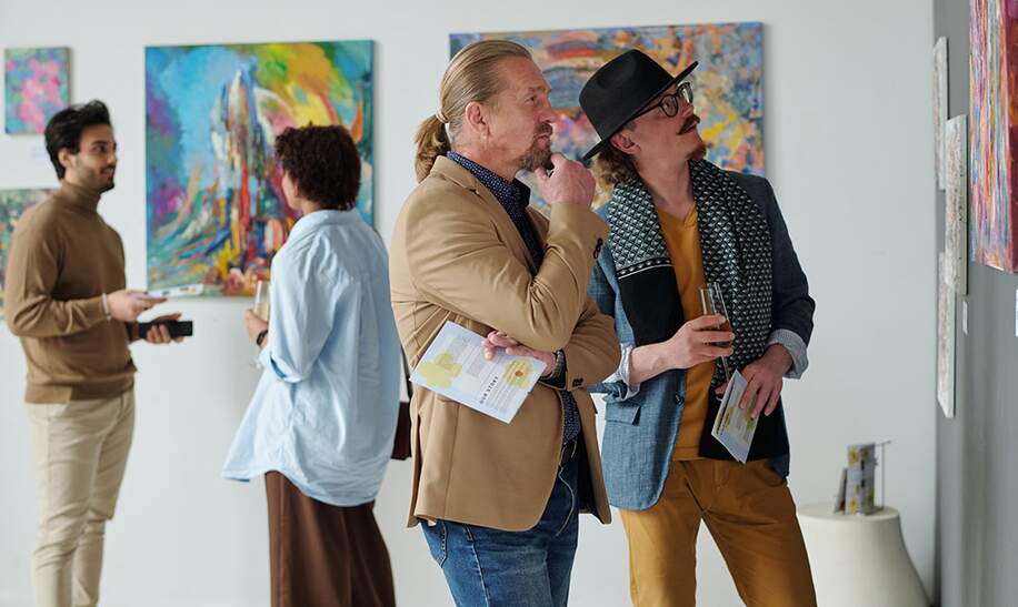 Menschen betrachten Gemaelde an der Wand und diskutieren darueber, waehrend sie die Ausstellung moderner Kunst in der Galerie besuchen | © Gettyimages.com/shironosov