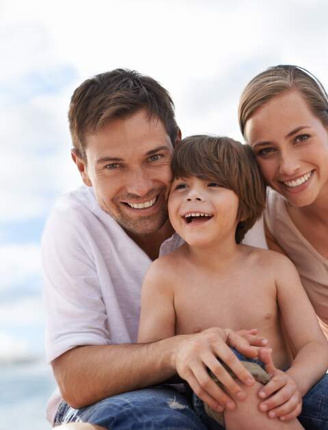 Die Eltern sitzen mit ihrem Sohn am Strand und umarmen sich | © Gettyimages.com/PeopleImages