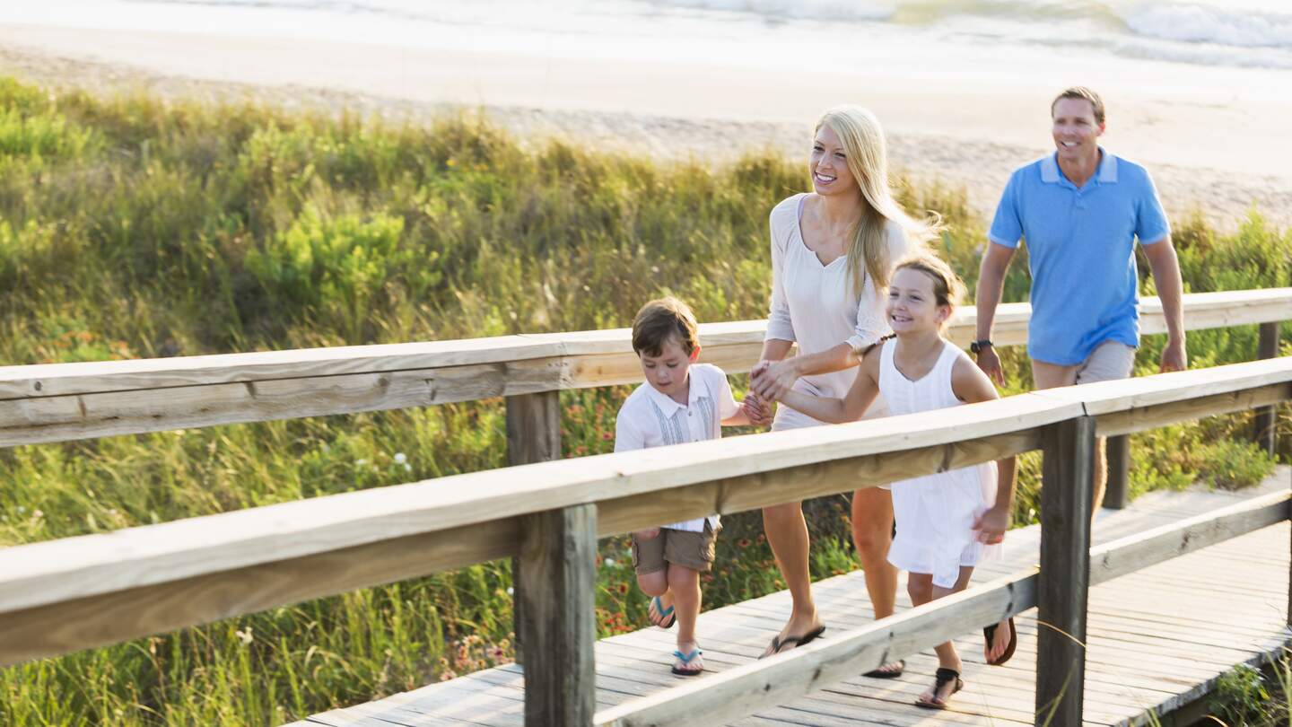 Familie laeuft auf der Strandpromenade. Die Kinder halten die Haende der Mutter | © Gettyimages.com/kali9