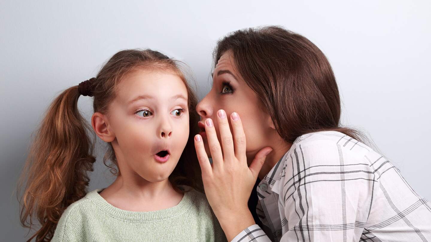 Mutter, die ihrem ueberraschend suessen Maedchen auf blauem Hintergrund die geheimen Informationen ins Ohr fluestert | © Gettyimages.com/Nastia11