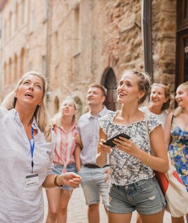 Kleine Reisegruppe auf historischem Stadtrundgang. Sie hoert einem Reiseleiter zu, der ueber die Architektur und die Geschichte spricht. | © Gettyimages.com/SolStock