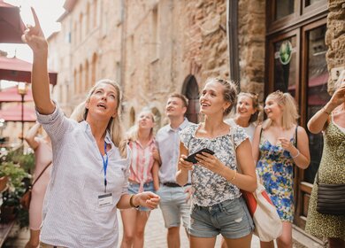 Kleine Reisegruppe auf historischem Stadtrundgang. Sie hoert einem Reiseleiter zu, der ueber die Architektur und die Geschichte spricht. | © Gettyimages.com/SolStock