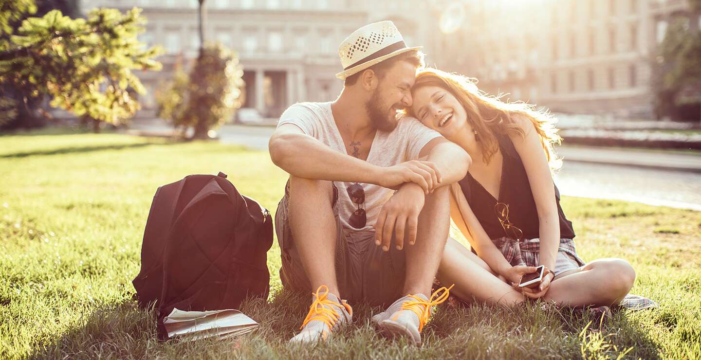 Junges Touristenpaar, das eine fremde Stadt erkundet. Im Park auf Gras sitzen und die Karte auf dem Smartphone ueberpruefen. Tragen Sie Freizeitkleidung und Rucksaecke. Genießen Sie den schoenen sonnigen Tag. | © Gettyimages.com/svetikd