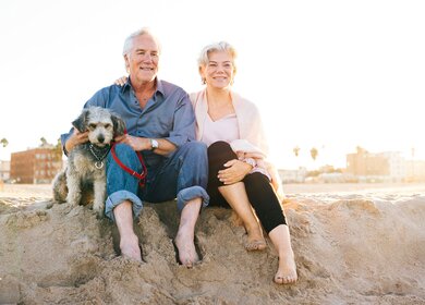 Seniorenpaar sitzt mit Hund im Sand am Strand | © Gettyimages.com/Weekend Images Inc.