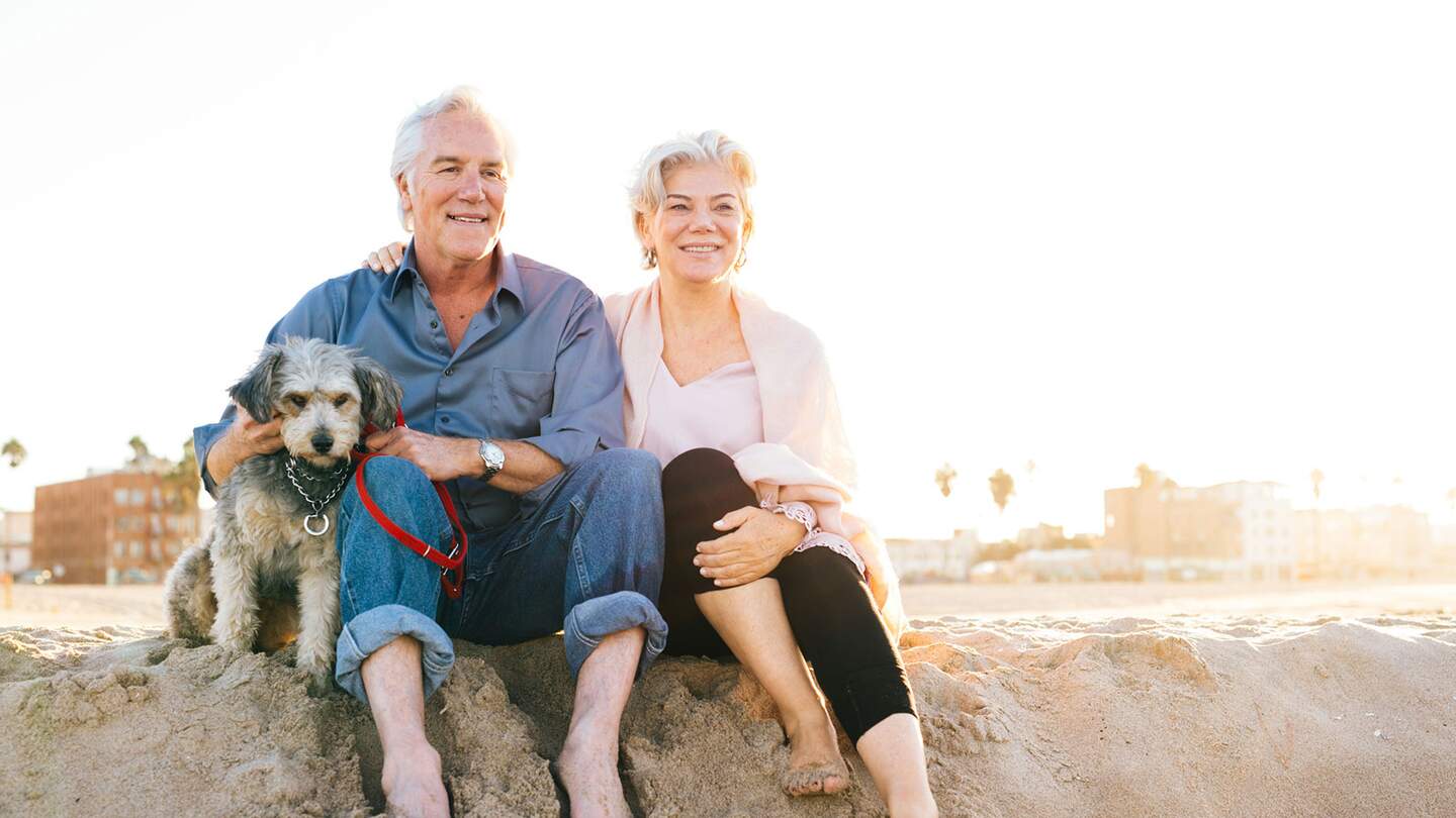 Seniorenpaar sitzt mit Hund im Sand am Strand | © Gettyimages.com/Weekend Images Inc.