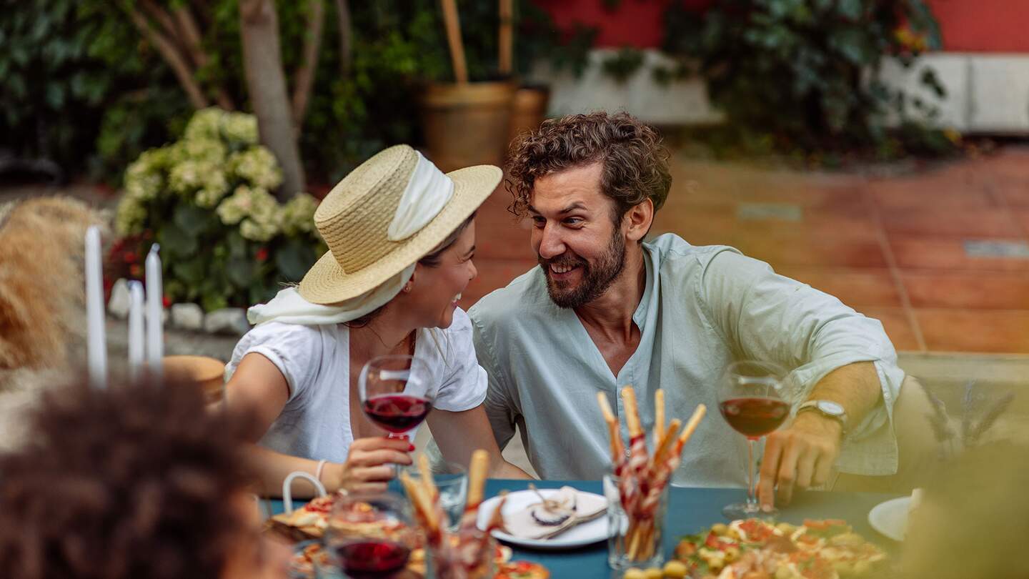 Paar sitzt mit Freunden am Esstisch und geniesst den Nachmittag im Hinterhof | © Gettyimages.com/Dimensions