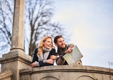Paar mit Stadtplan steht auf einem Aussichtspunkt und schaut nach rechts | © Gettyimages.com/MStudioImages
