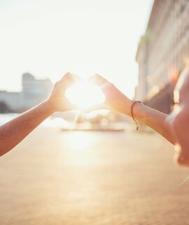 Junges Paar zeigt gemeinsam den Umriss eines Herz-Symbols gegen die untergehende Sonne | © Gettyimages.com/martin-dm