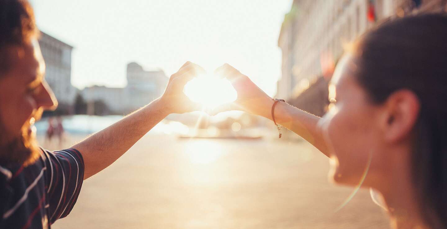 Junges Paar zeigt gemeinsam den Umriss eines Herz-Symbols gegen die untergehende Sonne | © Gettyimages.com/martin-dm