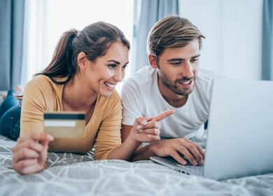 Paar bucht online auf Bett | © GettyImages.com/VioletaStoimenova