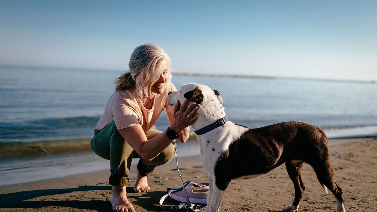 Ältere Frau streichelt ihren Hund am Strand | © Gettyimages.com/wundervisuals