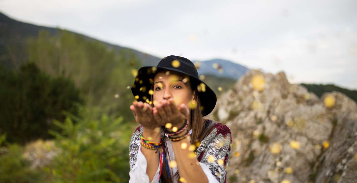EIne Frau entspannt sich auf dem Berg und blaest Konfetti | © Gettyimages.com/South agency