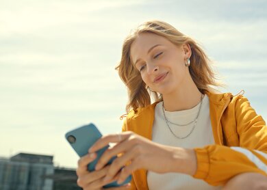 Frau sitzt auf einer Dachterrasse und schaut auf ihr Handy | © Gettyimages.com/marcovdm