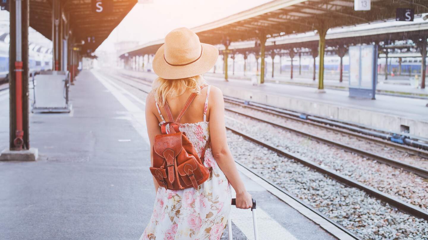 Junge Frau mit Rucksack im Sommer auf einenZug am Bahnhof wartend. | © GettyImages/Anna Berkut