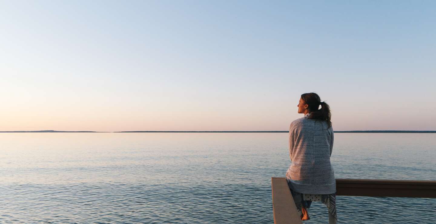 Nachdenkliche Frau sitzt am Wasser und blickt in die Ferne und genießt die ruhige Atmosphäre | © Gettyimages.com/AscentXmedia