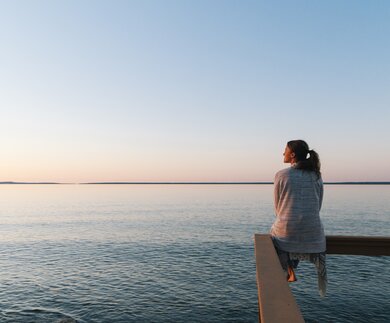 Nachdenkliche Frau sitzt am Wasser und blickt in die Ferne und genießt die ruhige Atmosphäre | © Gettyimages.com/AscentXmedia