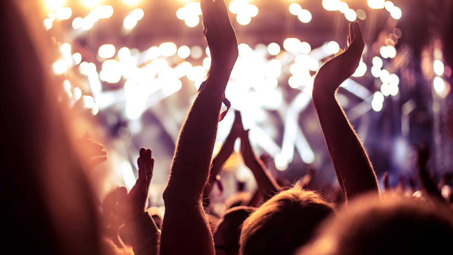 Eine Menge Leute, die feiern und feiern mit den Händen in der Luft zu einem fantastischen Dance musik | © Gettyimages.com/bernardbodo