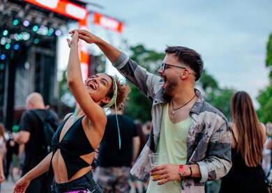 Ein junges Paar tanzt auf einem Konzert an einem Sommertag, sie halten Haendchen und haben Spass | © Gettyimages.com/dimensions