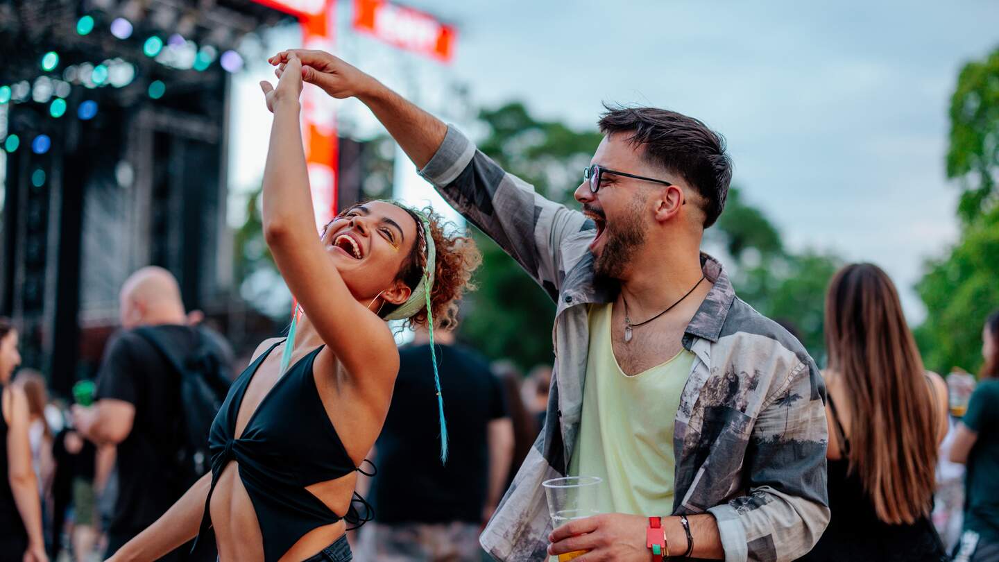 Ein junges Paar tanzt auf einem Konzert an einem Sommertag, sie halten Haendchen und haben Spass | © Gettyimages.com/dimensions