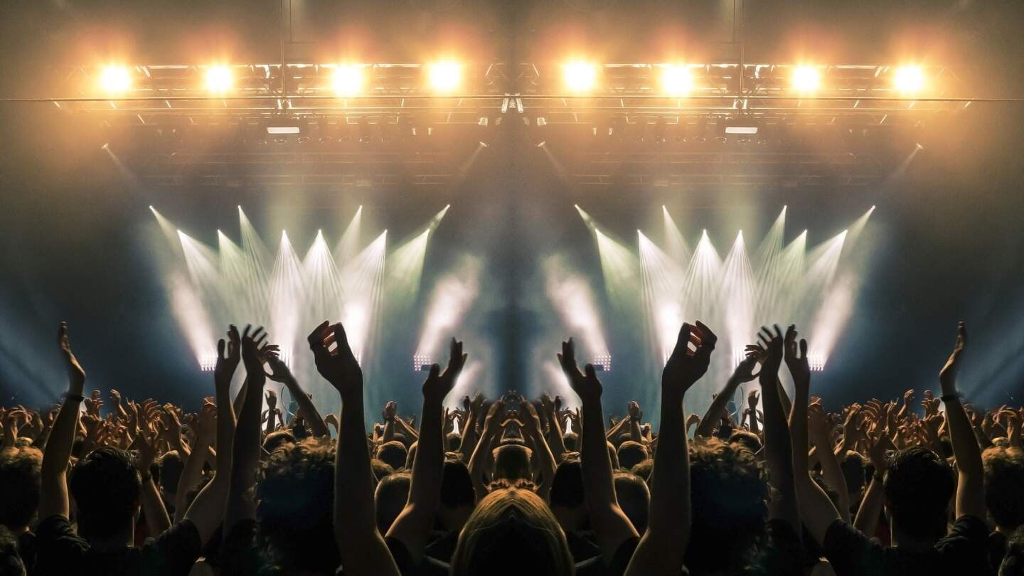 Konzertbuehne, Menschen winken und klatschen, Silhouetten sind sichtbar | © Gettyimages.com/cesareferrari