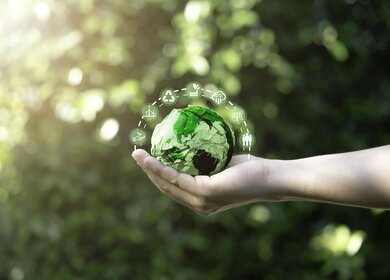 Mann hält grüne Erde mit Emojis drum herum | © Gettyimages.com/DilokKlaisataporn