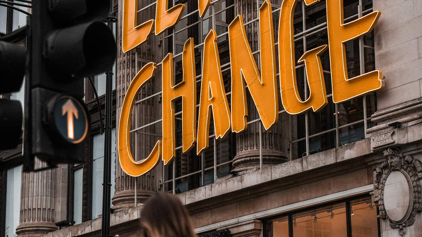 Eine Frau, die an einem Gebäude vorbeigeht, mit einem Schild mit der Aufschrift Let's change | © Unsplash/Brad Starkey