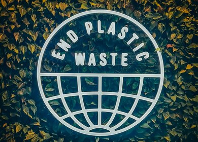 Beleuchteter Schriftzug Plastikmüll vermeiden vor Wand mit Blättern | © Unsplash/Ahmed Shabana