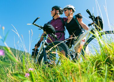 Ein Seniorenpaar steht mit Fahrraedern auf einer gruenen Wiese, schaut in die Ferne und ist aus der Untersicht zu sehen, der Himmel ist strahlend blau | © GettyImages.com/nullplus