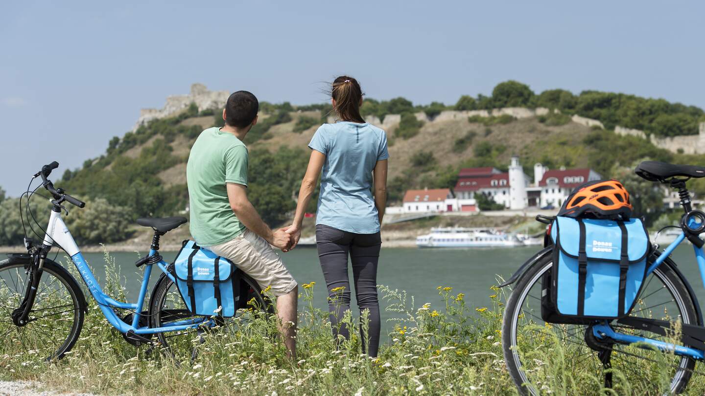 Ein Paar mit zwei Fahrrädern auf einer Wiese geparkt und in die Ferne blickend | © Donau Touristik/Zupanc