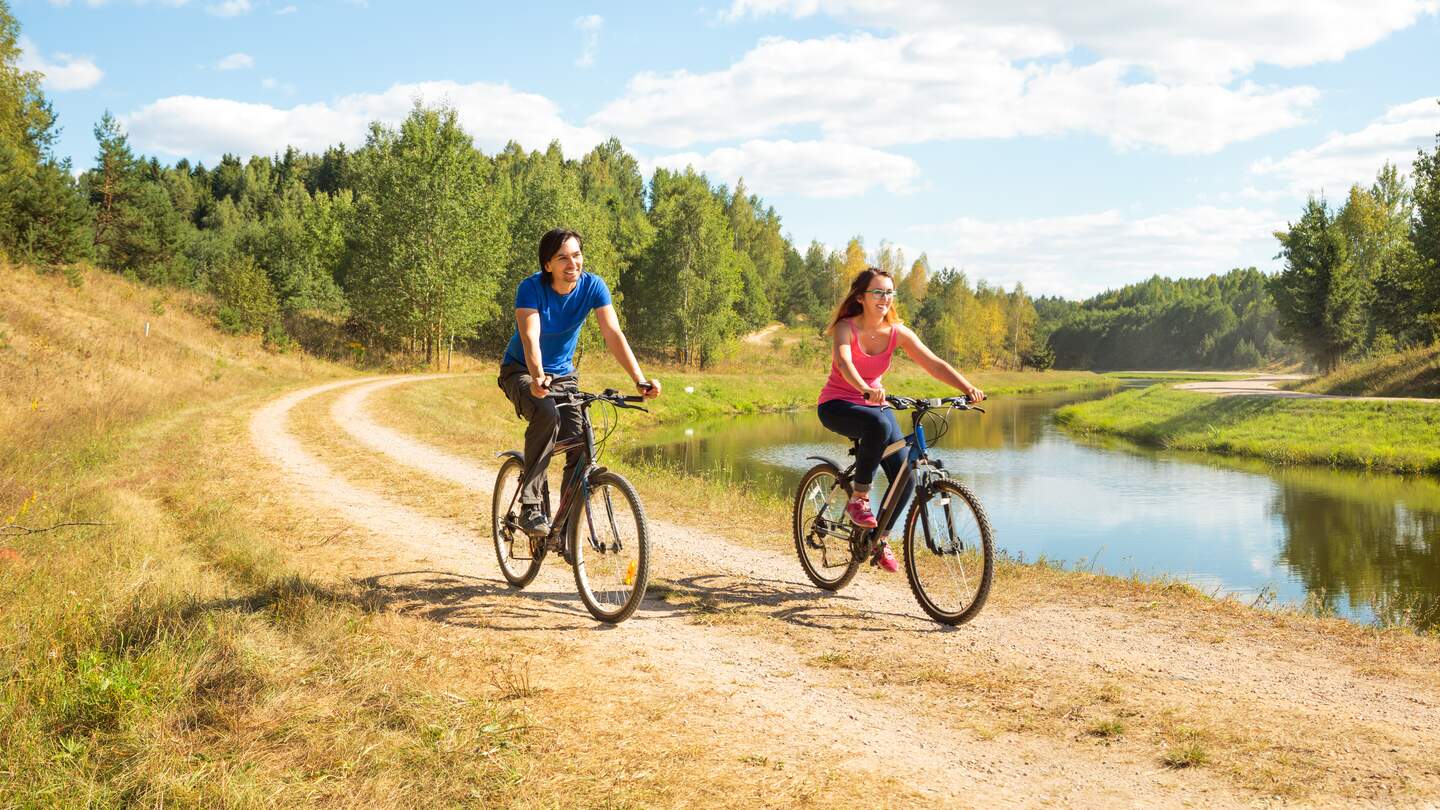 Paar bein Radfahren am Fluss bei warmen Wetter mit Sonnenschein | © GettyImages.com/brickrena
