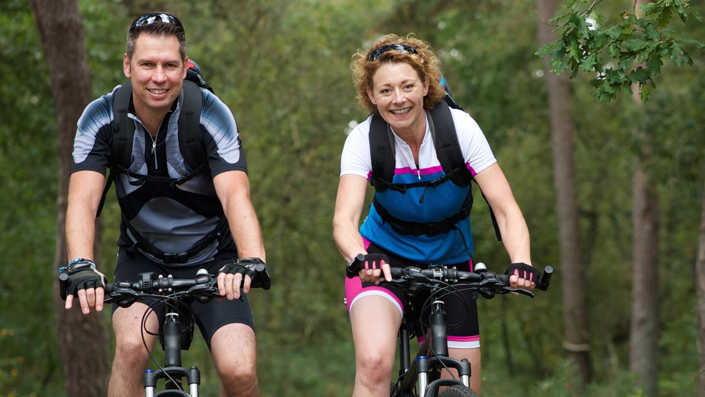 Paar faert mit kurzer, sportlicher Kleidung ueber eine Waldweg mit Baeumen auf beiden Seiten | © GettyImages.com/m-imagephotography