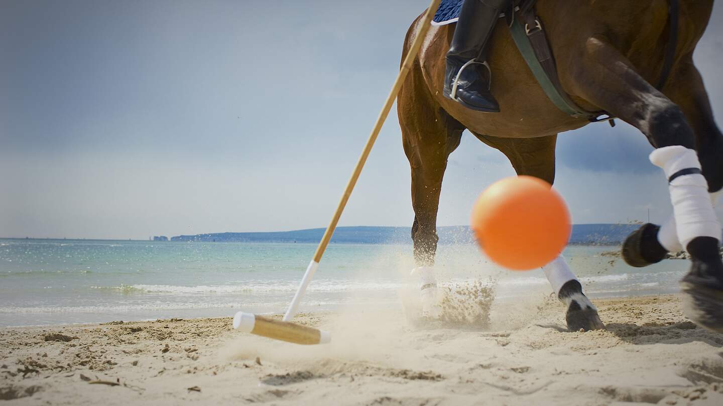 einen Poloschlaeger,der einen orngefarbenen Ball auf einem Sandstrand trifft | © gettyimages.com/SLR911